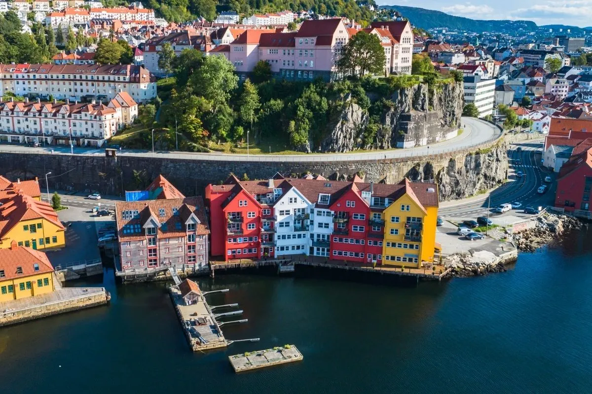 Geschilderde houten pakhuizen aan het water in Bergen, met een jachthaven en een rotswand erachter