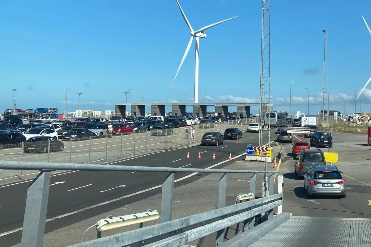 Auto's in de rij in de opstelvakken bij de terminal, met een windturbine erachter