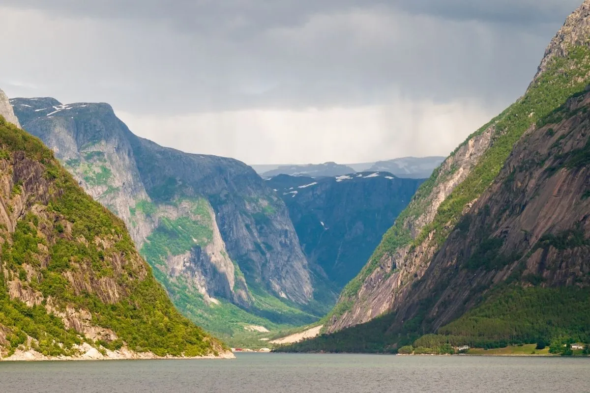 Een fjord met steile bergwanden en sneeuwvelden, onder een zware lucht